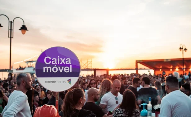 Placa de “Caixa móvel” com destaque para pagamentos cashless em um evento ao ar livre ao entardecer, com multidão e pessoas ao redor.