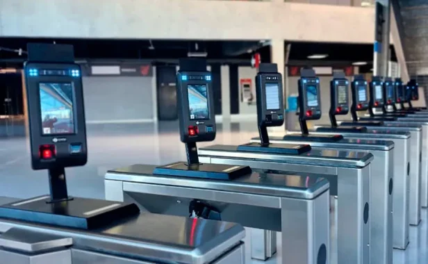 catraca reconhecimento facial: Catracas de acesso com leitores de reconhecimento facial em ambiente corporativo, com telas de interface e braços metálicos organizados em fila para controle de entrada.