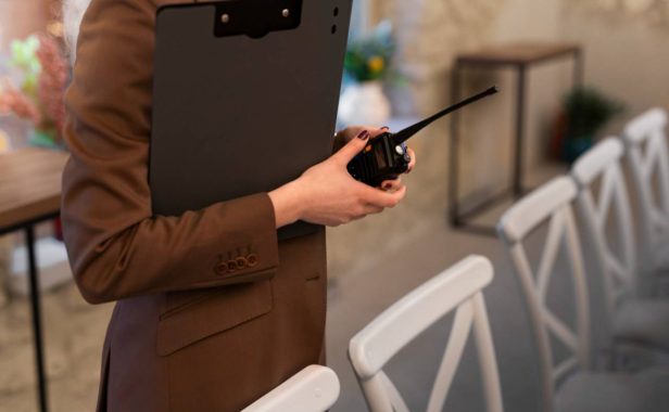 Mulher de blazer marrom segurando walkie talkie e prancheta pretos