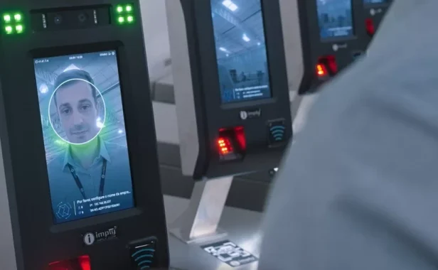 Painel de identificação facial com câmera e leitor de reconhecimento biométrico, exibindo o rosto de uma pessoa em uma tela circular, em ambiente de tecnologia.