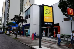 Painel digital em calçada urbana com pessoas passando